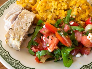 Close view on a plate with cooked red lentil, tomato salad and slices of steamed pork