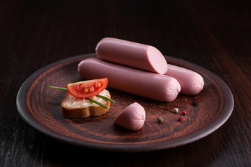 Sausage on a dark background in the plate and on the cutting board. Sausage with sauces and snacks. Onions, garlic, parsley, dill, olives, cheese, tomatoes, cucumbers, basil, eggs with sausage.
