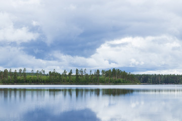 Rainclouds over a Swedish lake inside a forest with the water creating a mirror reflection in the water of the clouds and trees. 