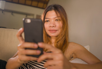 young attractive and relaxed 30s Asian Indonesian woman lying comfortable with mobile phone at home living room couch using internet social media or online dating app