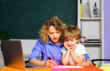 Education, elementary school, learning, math and people concept. Teacher helping young boy write lesson. Happy teacher helping pupil at elementary school. Little schoolboy with teacher in classroom.