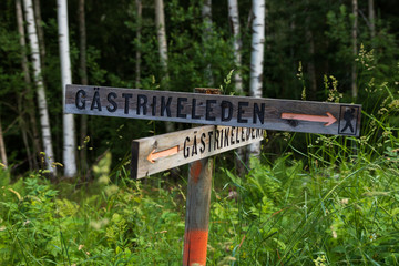 Sign for Gästrikeleden (path in Gästrikland, Sweden) in a forest in Gästrikland, Sweden during an early morning in summer. Showing the way while walking in the forest. 