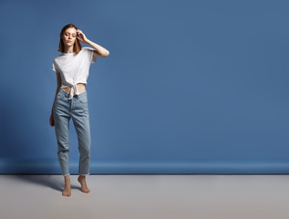 Portrait of the young modern woman. The serious beautiful thin brunette with equal hair in youth clothes. Blue background