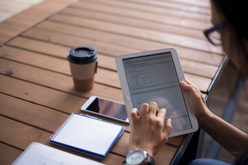 Women's hands with neat manicure and large wristwatch, work with gadgets, tablet, smartphone, papers on a wooden table.