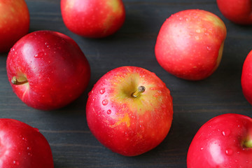 Heap of fresh ripe red apple with water droplets scattered on dark brown wooden table