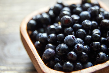 Bilberries in a bowl on brown wooden background, many fresh dark blue berries on table (European blueberries)