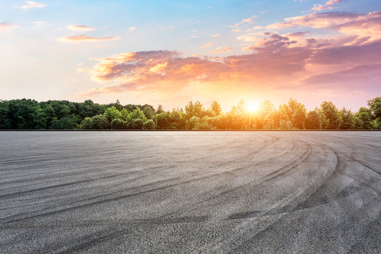 Asphalt race track and green forest with beautiful clouds at sunset