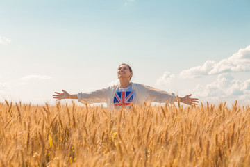 Naklejka na ściany i meble Young woman with raised arms in a t-shirt with a British flag in a wheat field