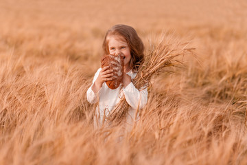 Happy child girl in white dress eats bread in a sunny field, summer outdoor lifestyle, cozy mood.