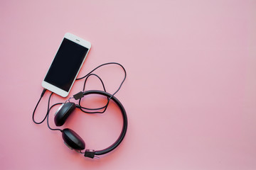 The music in the smart phone and headphones on a pink background.