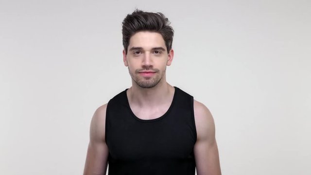 Excited young bearded sporty man in black shirt screaming and making winner gesture while looking at the camera over gray background isolated