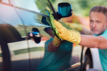 Man holding the microfiber in hand and polishes the car.