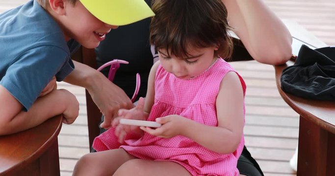 Child small girl looking at cellphone device screen, sister not letting brother get smartphone