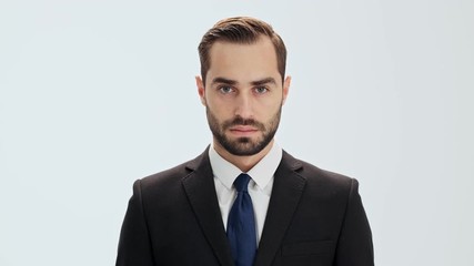 Serious young businessman in black suit and blue tie raising his head and looking at the camera over gray background isolated