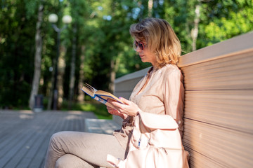A woman is reading a book on a park bench.