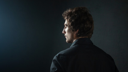 A young man with broad shoulders and a clear profile, in a dark shirt. Portrait from the back in half a turn.