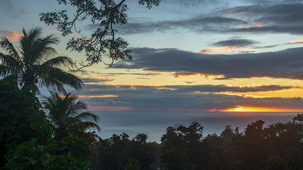 Fototapeta na wymiar Coucher de soleil avec nuage au milieu de la verdure tropicale