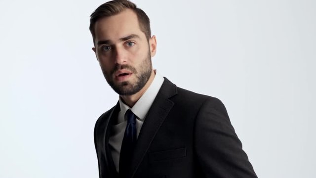 Attractive young businessman in black suit and blue tie feeling angry and rage while looking strict at the camera over gray background isolated