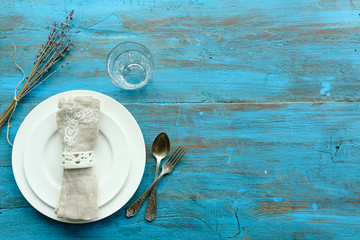 Spring place setting with vintage cutlery, plate with flowers, beige napkin on blue wooden background. Place under the inscription