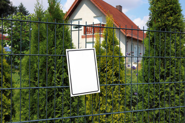 empty information plate on the fence against the background of a blurred house