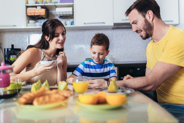 Family eating breakfast at kitchen table and using digital tablet.