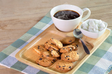 Raisin cookies and hot black coffee in white cup on wooden tray and apron cloth