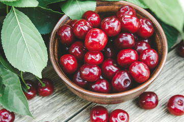 Cherry in a ceramic bowl and a branch of a cherry tree. Sweet organic berries on old wooden boards.