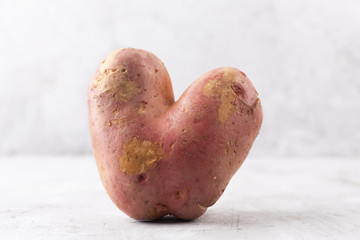 Ugly potato in the heart shape on a gray background. Funny, unnormal vegetable or food waste concept