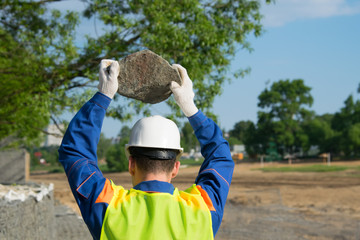 working in a white helmet, holding a stone with two hands, over the protected head, rear view