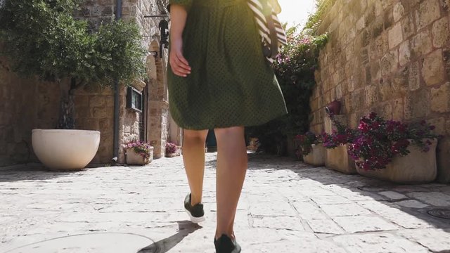 Young brunette with long hair walks down the street of Jaffa old city, slow motion. Girl tourist in green dress walks around historic old town.