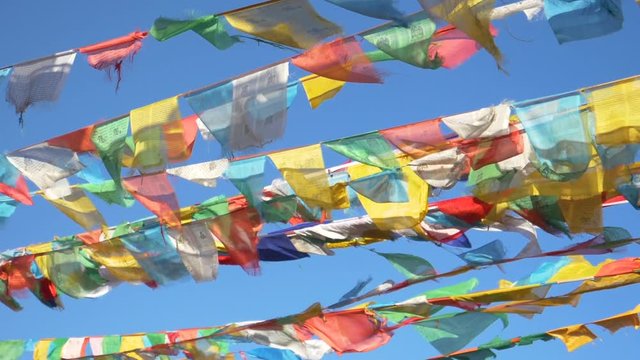 SLOW MOTION, CLOSE UP: Cinematic shot of vibrant buddhist flags waving above Tibet on a sunny day. Traditional multicolored flags hanging off of ropes spanning across Himalaya flap in the winds.