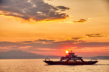 Ferry boat to the sea at sunset in the background of mountains and sun beams, run from Keramoti city to Thassos island in Greece