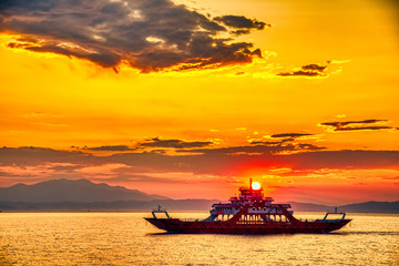Ferry boat to the sea at sunset in the background of mountains and sun beams, run from Keramoti city to Thassos island in Greece