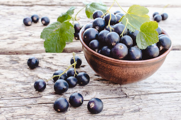 Fresh ripe currant berries in a bowl on wooden background near green leaves. Juicy fruits currants. Black currant