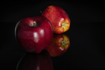 Group of two whole fresh apple red delicious one in front isolated on black glass