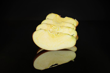 Group of four slices of fresh apple red delicious layered vertically isolated on black glass