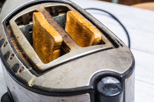 Dirty old toaster with bread on a white wooden background.