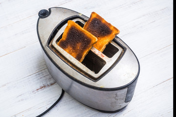 Dirty old toaster with burnt, overdone bread on a white wooden background. Broken, defective kitchen appliances.
