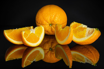 Group of one whole one quarter three slices of fresh sweet orange isolated on black glass