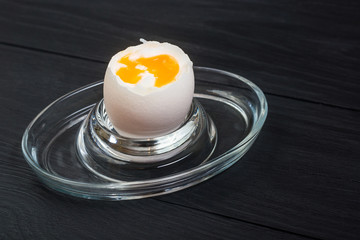 Boiled soft-boiled chicken egg on a black wooden background.