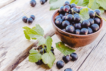 Fresh ripe currant berries in a bowl on wooden background near green leaves. Juicy fruits currants. Black currant