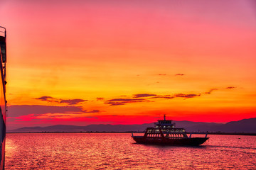 Obraz premium Ferry boat to the sea at sunset in the background of mountains and sun beams, run from Keramoti city to Thassos island in Greece