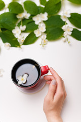 female hands holding a red cup of green tea with spring jasmine flowers on the white table background