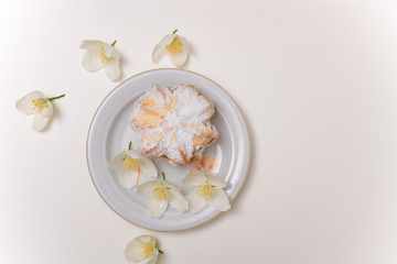 cake with jam and powdered sugar on the plate with spring jasmine flowers on the white background