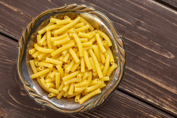 Lot of whole raw pasta macaroni in old iron bowl flatlay on brown wood