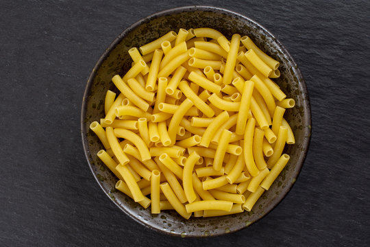 Lot of whole raw pasta macaroni on grey ceramic plate flatlay on grey stone