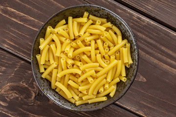 Lot of whole raw pasta macaroni on grey ceramic plate flatlay on brown wood