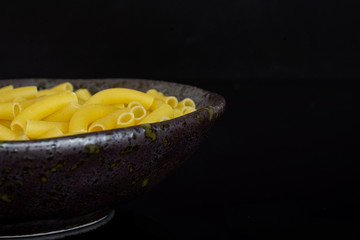 Lot of whole raw pasta macaroni on grey ceramic plate isolated on black glass