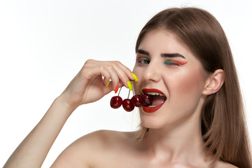 Closeup portrait of a beautiful young woman with bright color make-up holding strawberry near the face.