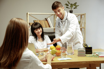 Smiling nutritionists showing a healthy diet plan to patient. Young woman visiting a doctor for...